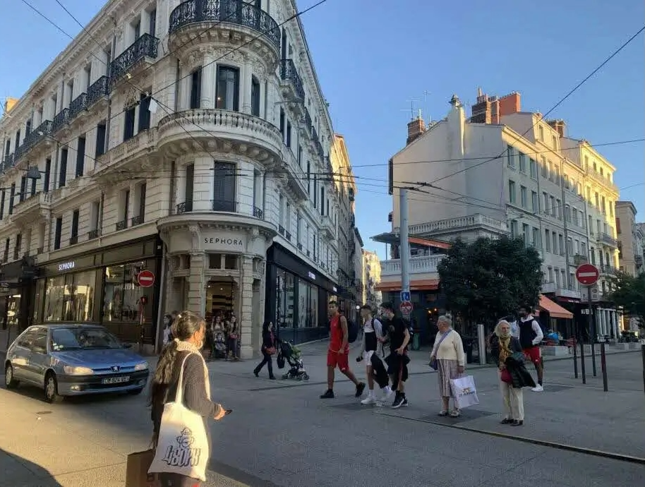 Des personnes marchent dans une rue animée d'une ville, entourées de bâtiments et de commerces.