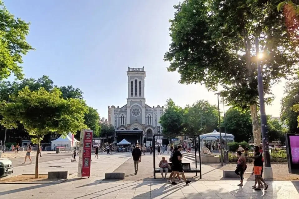 Des personnes se promènent dans une plaza avec une église en arrière-plan.